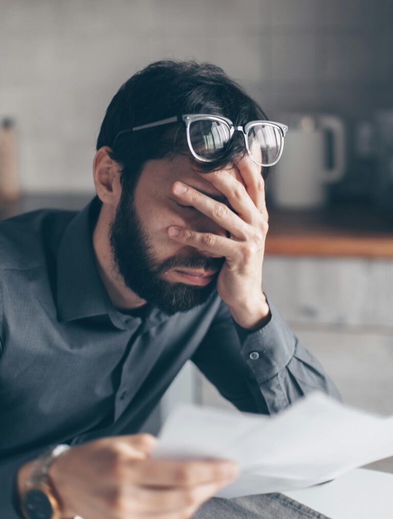 a man with glasses covering his face overwhelm by debt